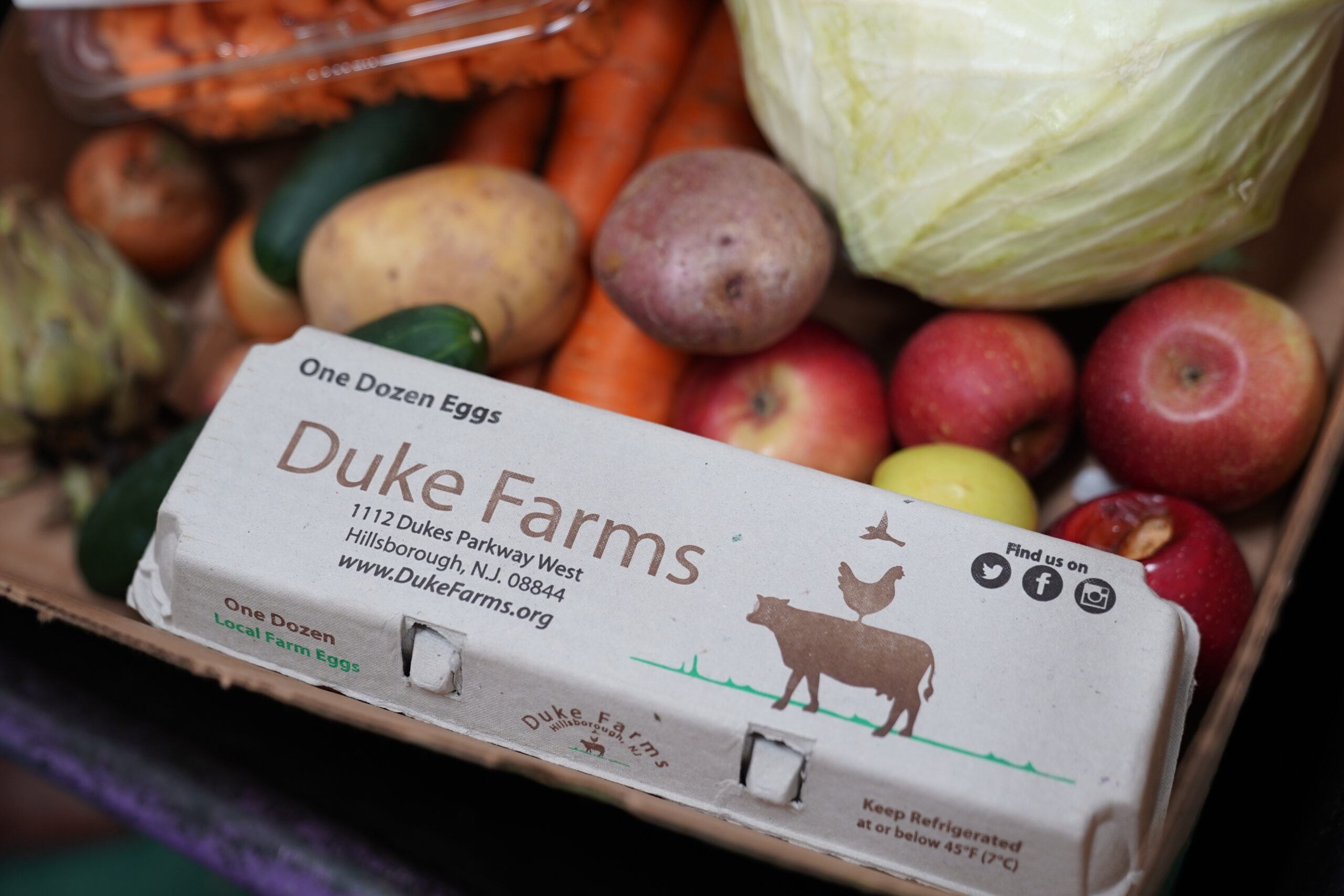 Picture of a carton of Duke Farms eggs, placed on top of other vegetables.